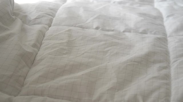 Hands bedding white blanket with natural light from window, slow motion