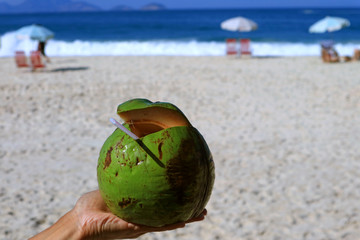 Fresh young coconut on man's hand with blurry sunshine beach in background