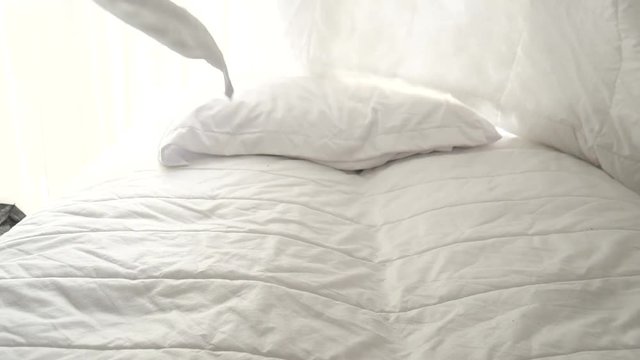 Hands bedding white blanket with natural light from window, slow motion