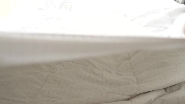 Hands bedding white blanket with natural light from window, slow motion