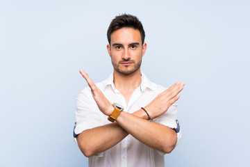 Handsome young man over isolated blue background making NO gesture