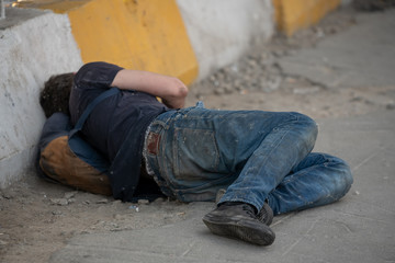 homeless man, tramp, lying in dirty ragged clothes on the road near the fence