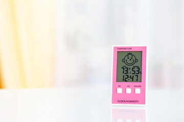 Pink electronic hygrometer on white table in front of the window. Fahrenheit mode