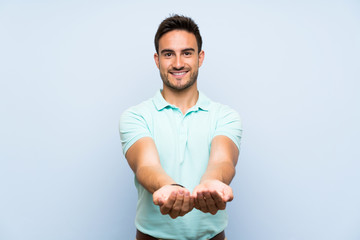 Handsome young man over isolated background holding copyspace imaginary on the palm to insert an ad