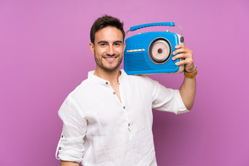 Handsome young man over purple background holding a radio