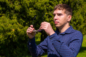 Portrait of a man in sunglasses and blue shirt standing outside in park