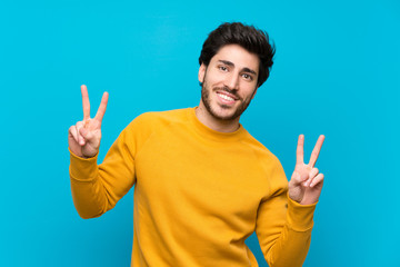 Handsome over isolated blue wall showing victory sign with both hands