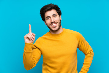 Handsome over isolated blue wall showing and lifting a finger in sign of the best