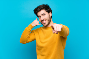 Handsome over isolated blue wall making phone gesture and pointing front