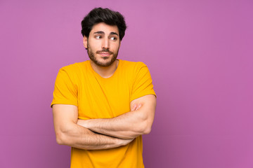 Handsome over isolated purple wall making doubts gesture while lifting the shoulders