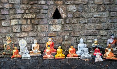 Strange and damaged figurines of Buddha of the different size along brick wall