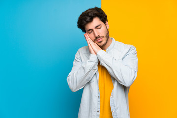 Handsome over isolated colorful background making sleep gesture in dorable expression