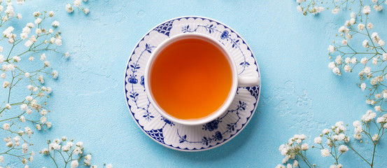 Cup of tea with fresh flowers on blue background. Top view. Copy space.