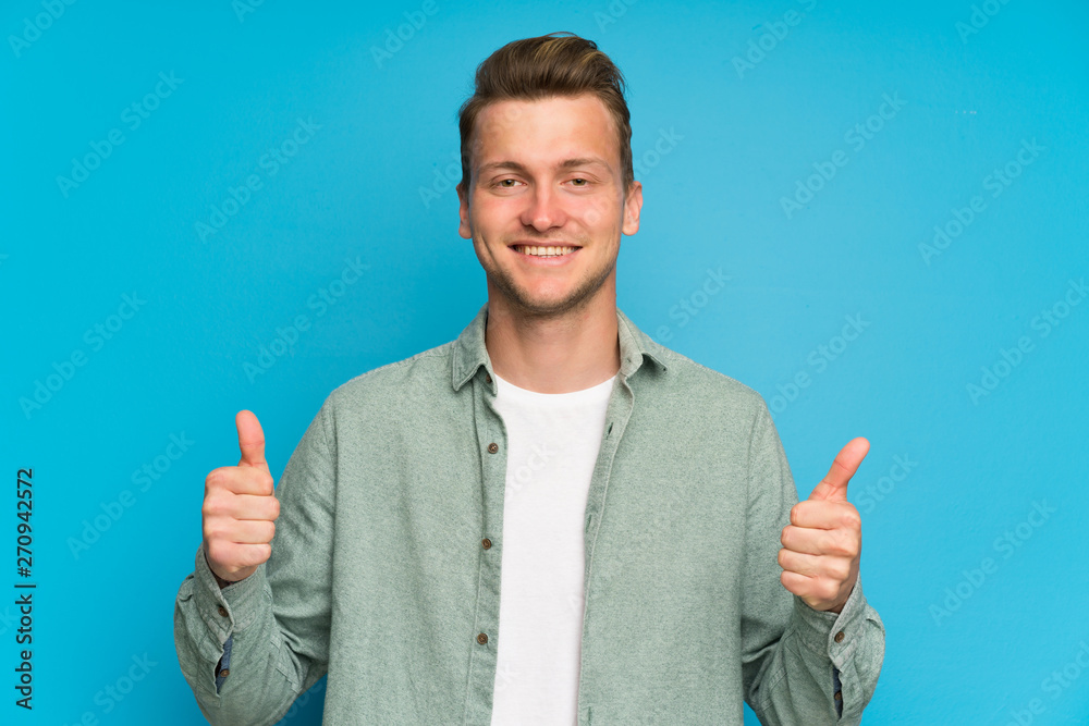 Wall mural blonde handsome man with green shirt giving a thumbs up gesture