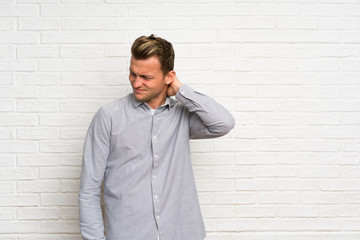 Blonde man over white brick wall with neckache