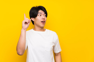 Asian man over isolated yellow wall intending to realizes the solution while lifting a finger up