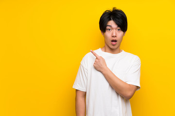 Asian man over isolated yellow wall surprised and pointing side