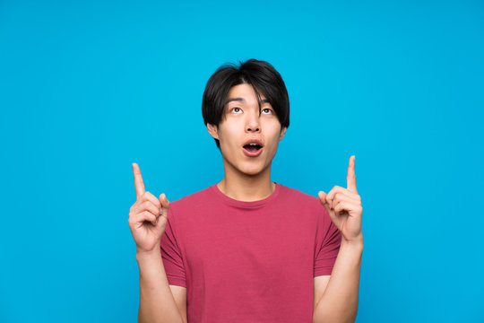 Asian Man With Red Shirt Over Isolated Blue Wall Pointing With The Index Finger A Great Idea