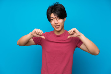 Fototapeta premium Asian man with red shirt over isolated blue wall proud and self-satisfied