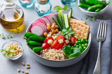 Healthy vegetarian salad. Buddha bowl. Quinoa, chickpea, tomatoes, pea, radish, cucumber, crackers. Grey background.