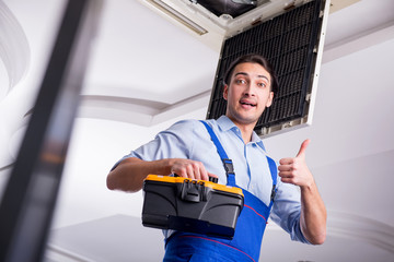 Young repairman repairing ceiling air conditioning unit 