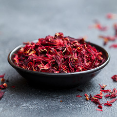 Fototapeta premium Hibiscus tea, flowers in black bowl. Slate background. Close up.