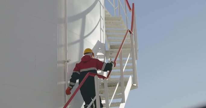 The engineer hurries up ladder of refinery tank for checking valves and safety systems