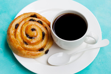 Fresh danish pastry with raisins with a cup of black coffee on blue table background.