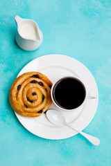 Fresh danish pastry with raisins with a cup of black coffee on blue table background. Top view.