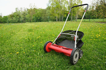 Red spindle lawn mower on lawn with cut grass part.