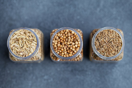 Spices assortment in jars, fennel, coriander, cumin seed. Grey stone background. Top view. Copy space.