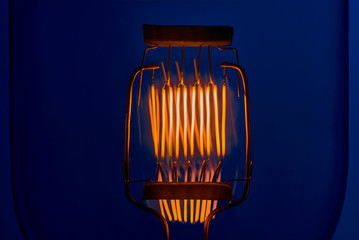 tungsten filament of high power incandescent lamp on blue background close up