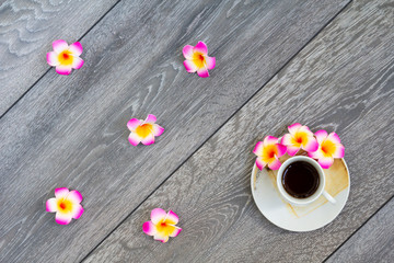 A mug of coffee on a wooden background, decorated with tropical flowers pink plumeria