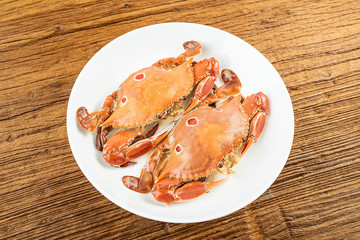 A dish of steamed three-pointed crab and seasoning sauce on a wooden table