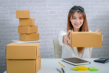 Beautiful young entrepreneur woman about an online business sitting working at home with a package box and taking note. Smiling and laughing happily.