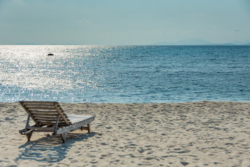 Wooden chairs on the white sandy beach with little waves, blue and bright blue sky.