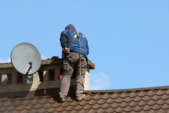 A technician on the roof of a house repairs a telescopic antenna for receiving and transmitting a radio signal. Dangerous profession and work at heights with insurance. Safety of human labor
