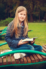 Obraz premium School-age girl sitting on a bench in the Park and reading something
