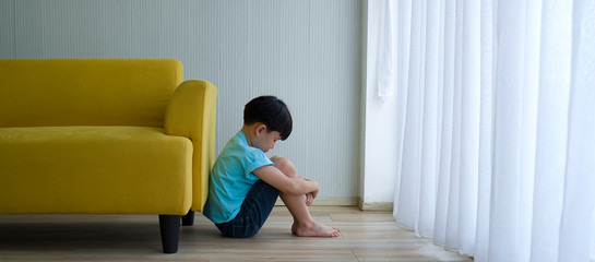 Little boy sitting beside yellow sofa at home. Child autism.