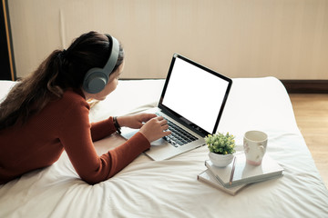 Mock up. Woman are listening to music and using laptop in the bed in morning time.