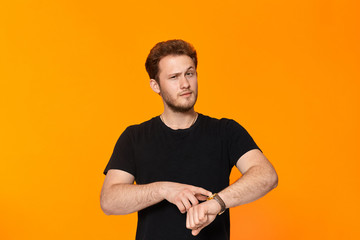 Studio shot of a bearded young man in black t-shirt pointing at the wristwatch.