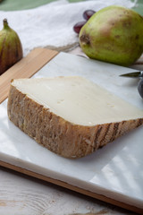 Piece of French cheese Tomme de Brebis made from sheep milk served as dessert with fresh figs and pears
