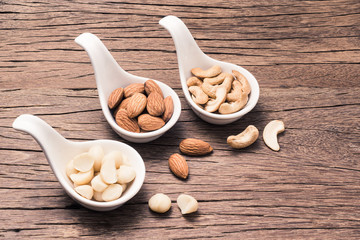Organic cashew nuts, almond nuts and macadamia nuts in spoon shape cup on space of old wood