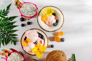 Balls of ice cream decoration flowers and berries in halves of coconut with green leaves. Summer tropical concept.