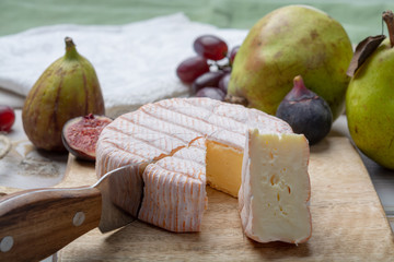 Round piece of French cheese Fleur Rouge made from cow milk served as dessert with fresh figs and pears