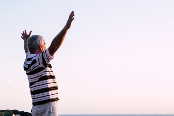 Happy of man standing alone with arms raised up during beautiful sunrise at the sunset. Enjoying with nature - retired man feels good and have fun - senior caucasian 60s freedom concept