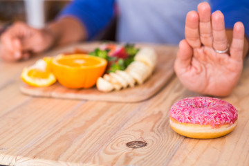 woman prefer vegetables and fruit at pink donut - two options - on the table - at home indoor - sane lifestyle and concept