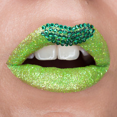 Green lips with sparkles covered with gemstones. Beautiful green lipstick on her lips, white teeth open mouth. Lip art