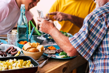 big table full of food life bread, meat, vegetables... - some people sitting next to the table eating and drinking vine and water - celebration - a lot of salad and all of types of food