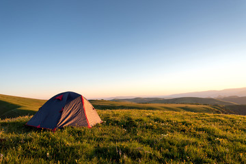 tourist tent stands on the green grass in the morning on a background of mountains